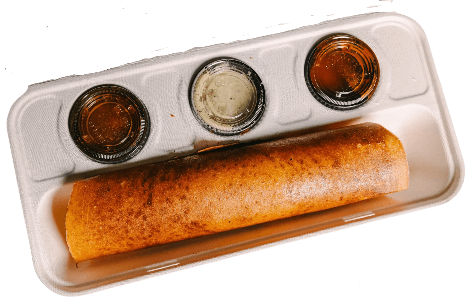A crisp golden dosa on a wooden tray with coconut chutney, sambar and chutney in black cups